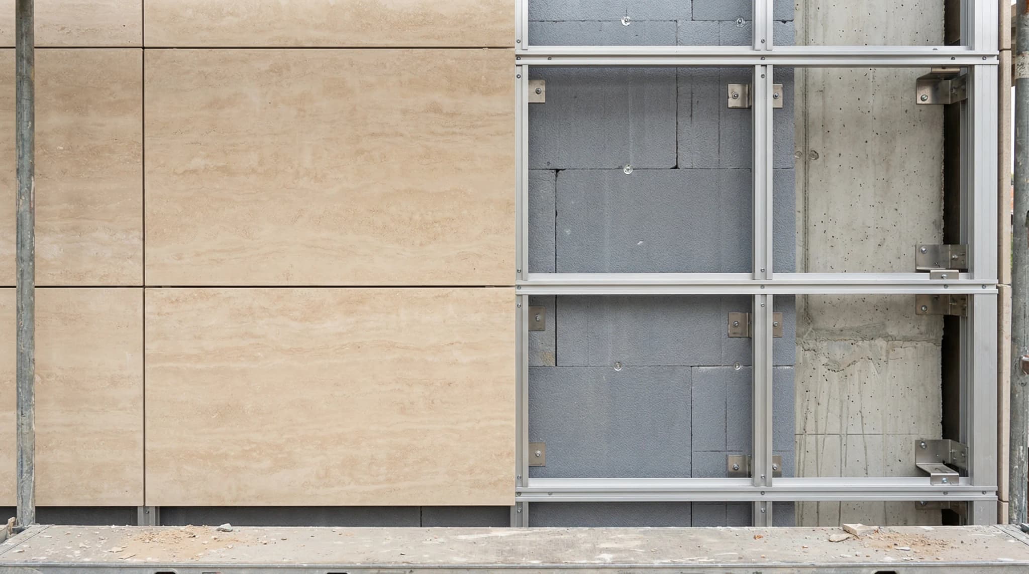 Ventilated travertine facade system during installation showing mounted stone panels alongside exposed aluminum rail subframe brackets and thermal insulation