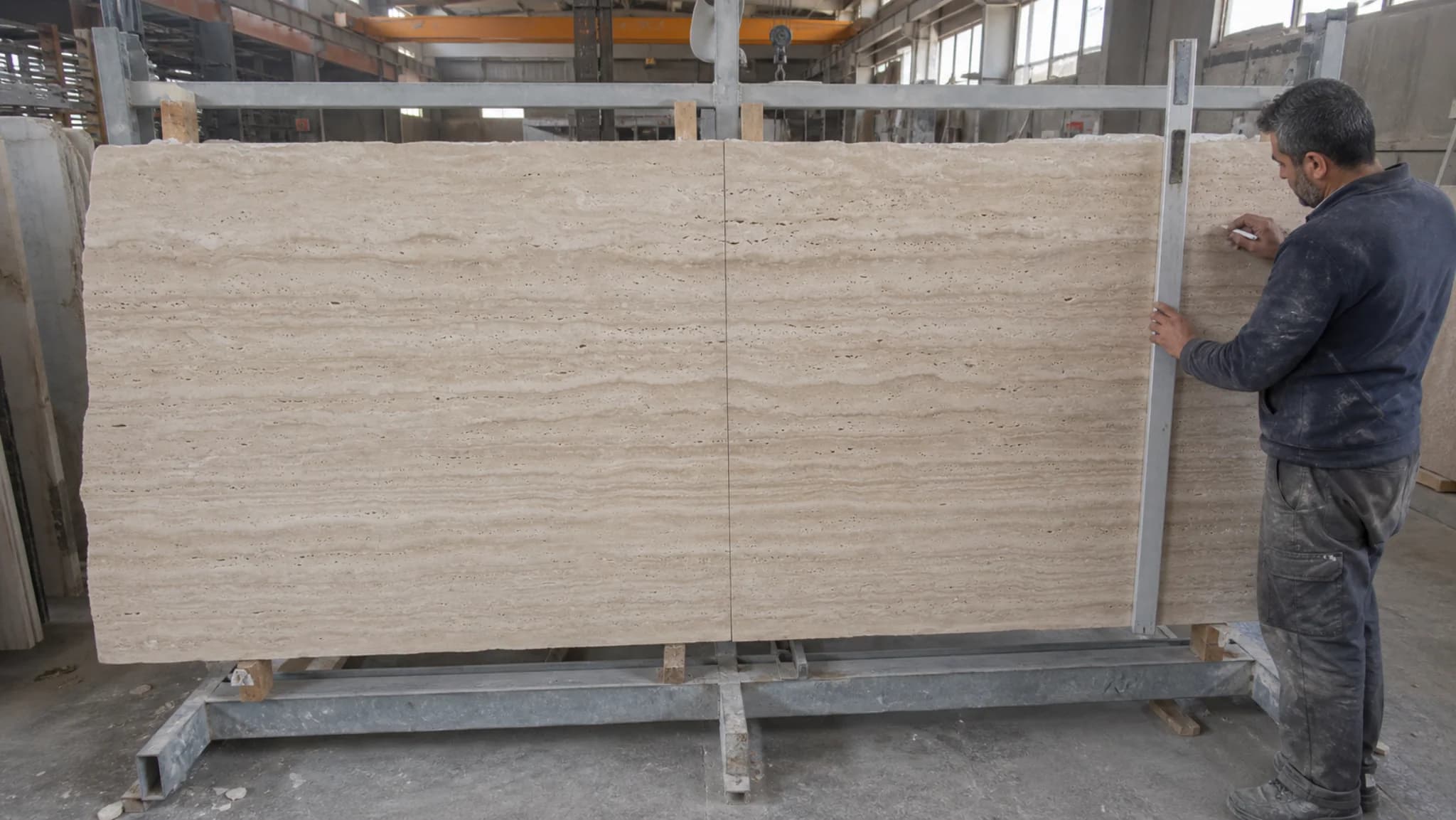 Stone technician checking the alignment of consecutive vein-cut travertine slabs during a factory dry layout