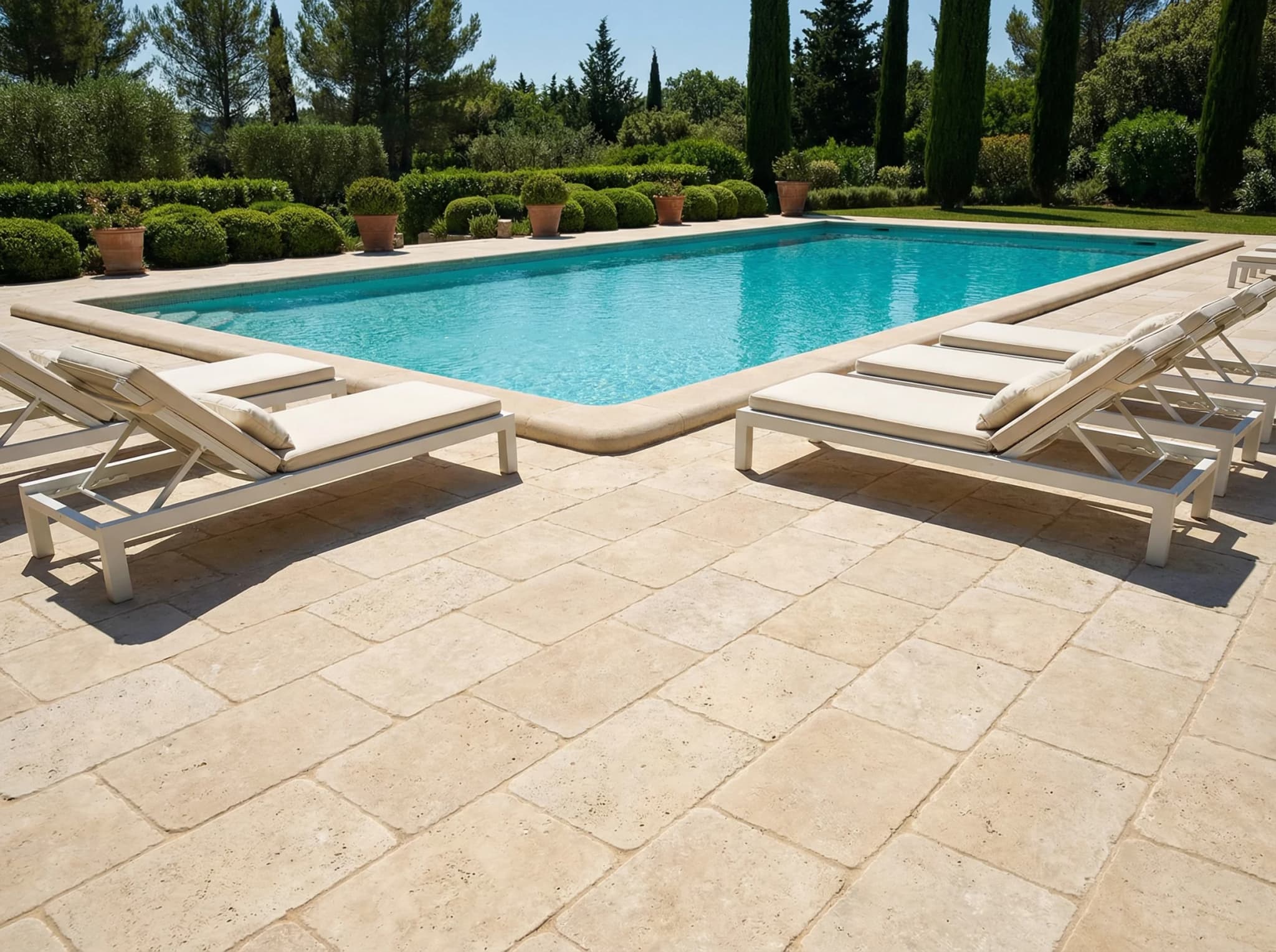 Luxury swimming pool surrounded by tumbled travertine pavers with bullnose coping, sun loungers, and Mediterranean cypress garden