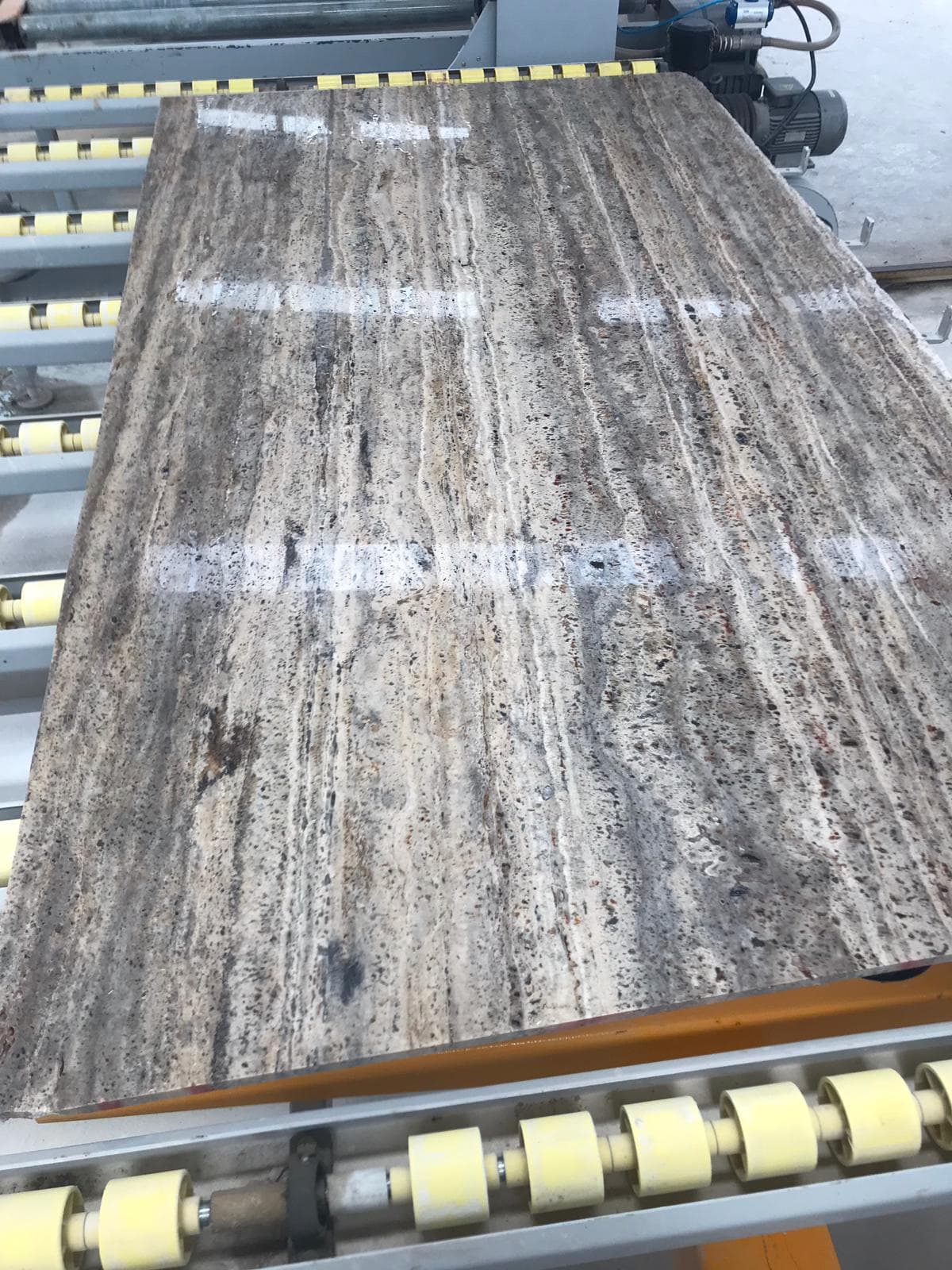 Vein-Cut Silver Travertine slab showing grey base with white veining and natural striations, polish finish on conveyor system Vein-Cut Silver Travertine slab showing grey base with white veining and natural striations, polish finish on conveyor system