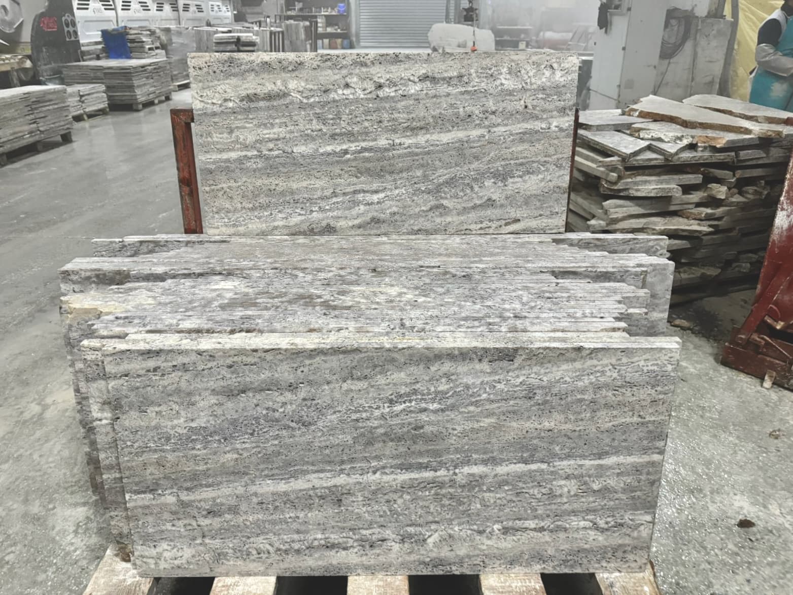 Vein-Cut Silver Travertine tiles with grey tones and linear vein patterns, displayed in stone yard warehouse setting Vein-Cut Silver Travertine tiles with grey tones and linear vein patterns, displayed in stone yard warehouse setting